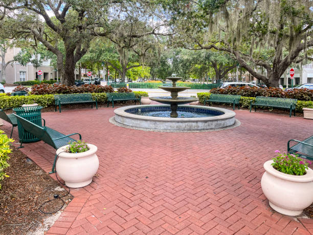 Fountain centered landscaped mini park with beautiful spanish moss covered southern oak trees, park benches, flower pots, and a perfect brick walkway