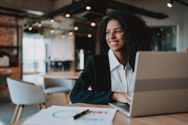 Young businesswoman using laptop at table looking to side