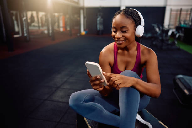 istock Happy black sportswoman using cell phone while exercising in a gym. 2161387451