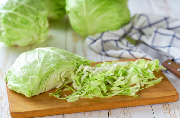 istock Whole and sliced fresh green cabbage on a white wooden table. 2161391295
