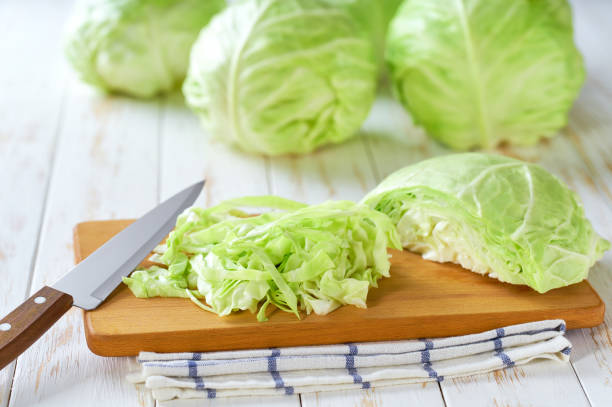 istock Whole and sliced fresh green cabbage on a white wooden table. 2161391301