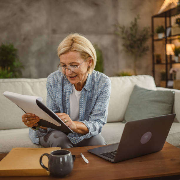 istock Mature woman work from home and compere data from laptop and clipboard 2161392489