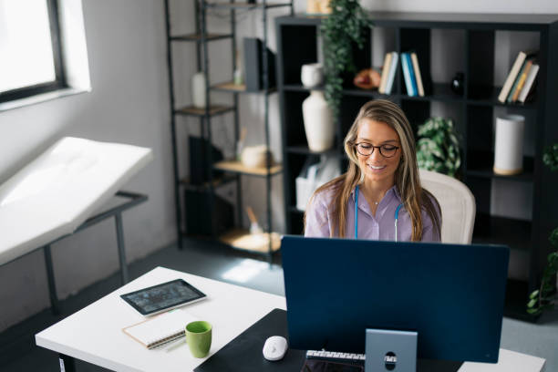 istock Happy female doctor using computer sitting at her desk in clinic 2161396096