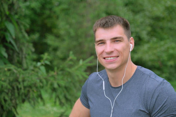 Handsome man looking at the camera while listening to music and smiling in nature