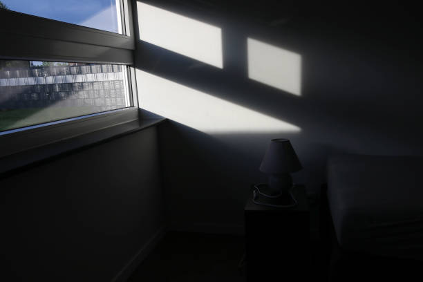 istock Sunlight falls through the window into a dark room with a lamp and bed 2161397638