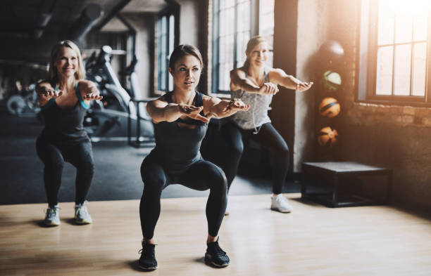 exercise, class and people with squat in gym for muscle development, workout and challenge. fitness, instruction and women with balance by sports mentor for healthy body, glutes strength and growth - treinar imagens e fotografias de stock