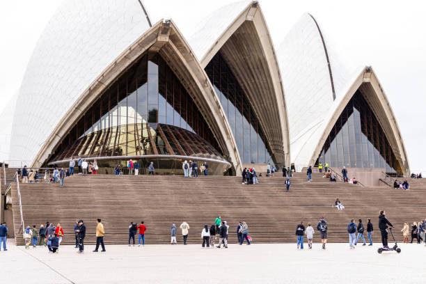 Sydney, Australia - July 06, 224: Front view of Sydney Opera House with a large group of tourists enjoying day in Sydney, Australia. The Opera House is a symbol of Australia. It has a unique, modern, expressionist design. The Opera House is located on the Circular Quay side of the Sydney Harbour.
