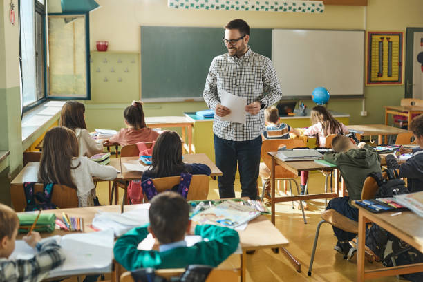 istock Young happy teacher talking to elementary students on a class in the classroom. 2161421682