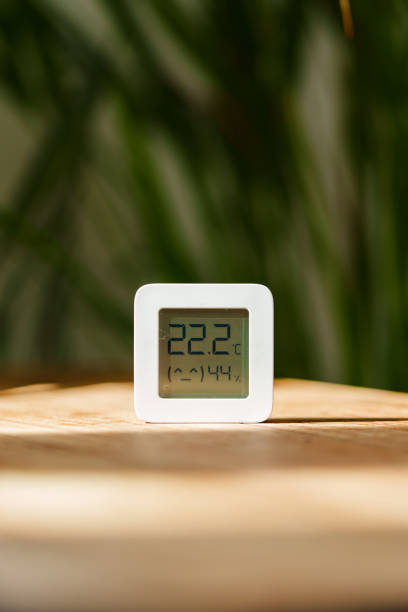 istock White Digital Thermometer Displaying Temperature and Humidity on Wooden Table With Green Plant in Background 2161431605