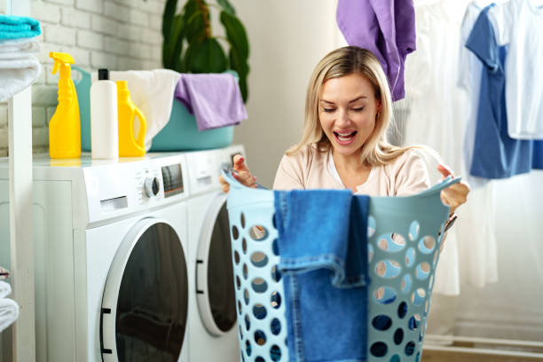 istock Woman Folding Laundry in a White Room With a Blue Laundry Basket 2161433763