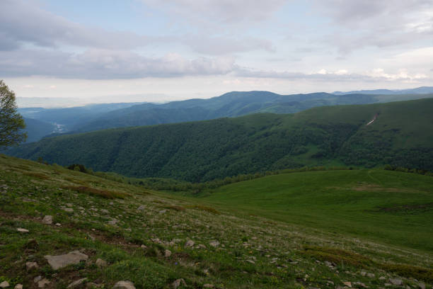 Expansive view of green hills and distant mountains under cloudy sky.