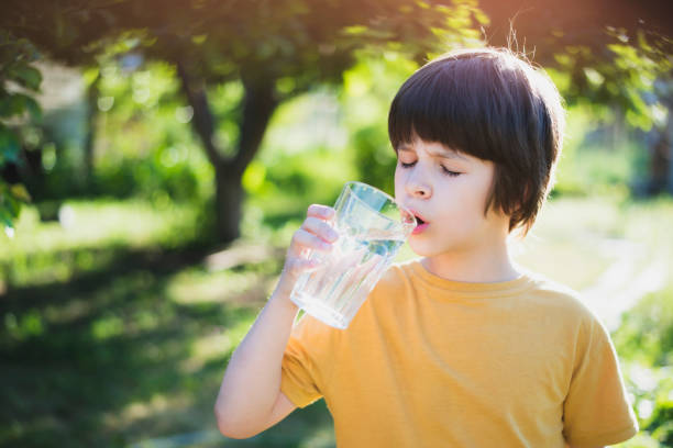istock A boy drinks water from a transparent glass in nature on a sunny day 2161441016