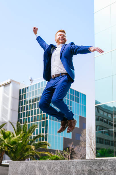 istock Triumphant redhead businessman jumping in a modern urban setting. 2161442737