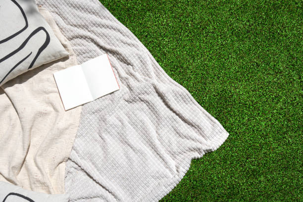 White blanket, cushion and book on green grass