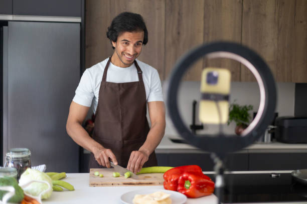istock Man filming a cooking tutorial in his kitchen, smiling and cutting vegetables. 2161448727