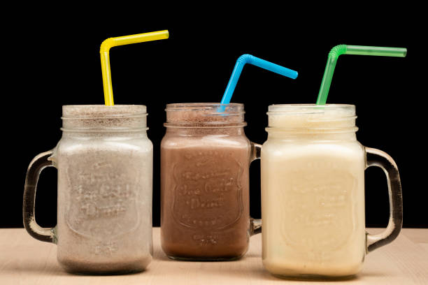 The three mason jar glasses filled with different smoothies and straws on a wooden table against black background