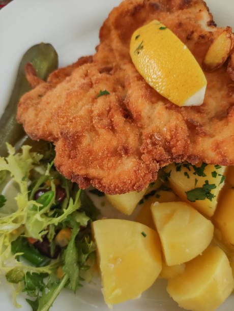 Fried pork schnitzel served with boiled potatoes, a side salad, and lemon wedge.