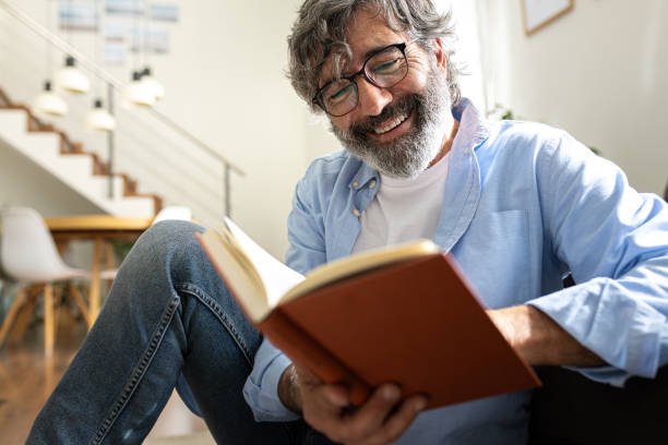 Happy mature man with glasses relaxing at home reading a book.
