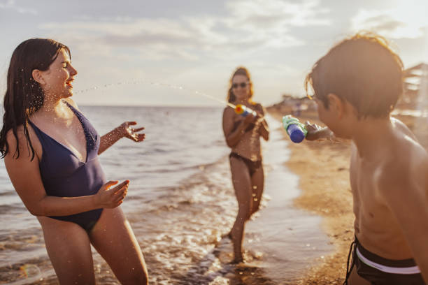 Engaging in a lively water gun fight, kids and adults are having a blast on the sunny beach with splashes of water and joy shining brightly as the waves roll in.