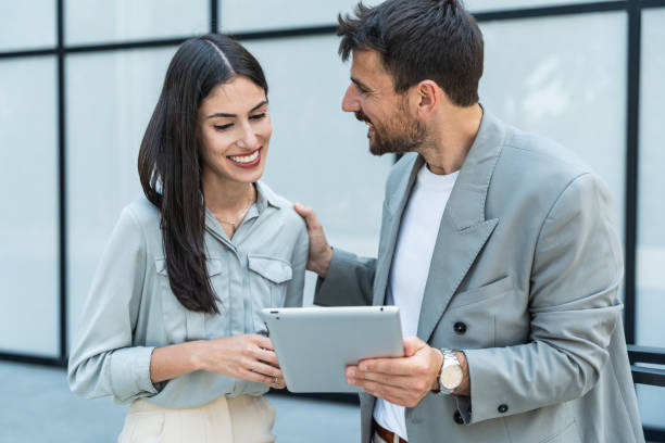 istock Two coworkers using a digital tablet and talking while standing outside. Modern business colleagues chatting together in front of office building on their way to work. Businesspeople collaboration 2161456632