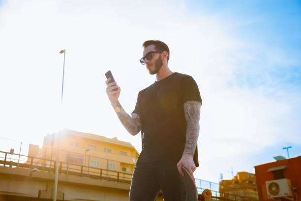 istock Tatooed young man walking in the city using smartphone 2161460488