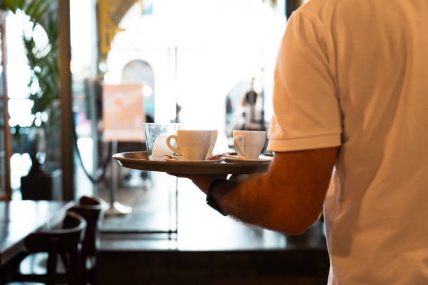 Waiter carrying coffees to a table with tray in one hand.