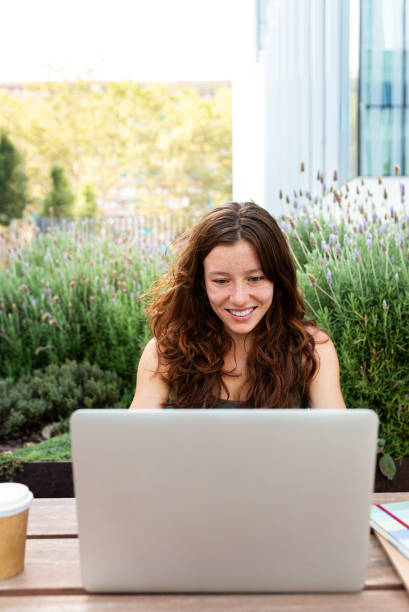 istock Front view of happy young redhead female university student using laptop outdoors sitting on table studying. Vertical 2161463551