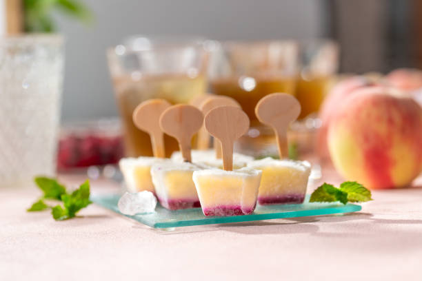 Homemade raspberries and peach popsicles on a pink background.