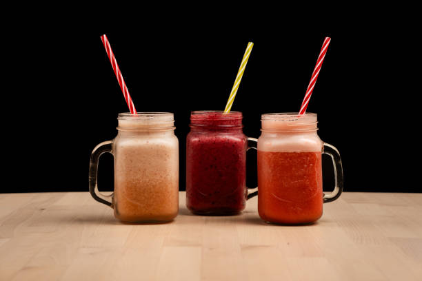 The tree mason jar glasses filled with different smoothies and straws on a wooden table