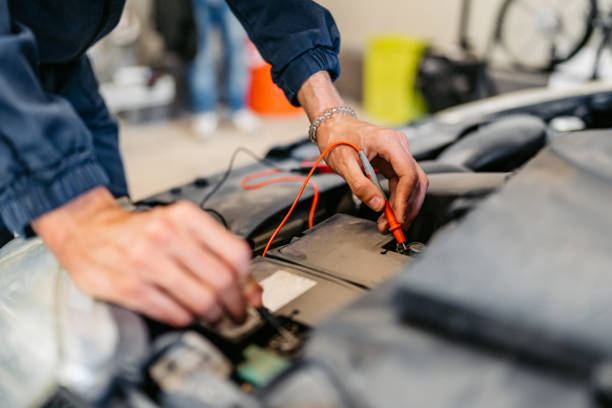 Young male car mechanic checking voltage on a car battery he is working on in his garage.