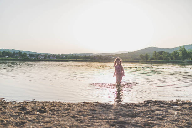 A beautiful view of a little girl entering the lake at sunset.