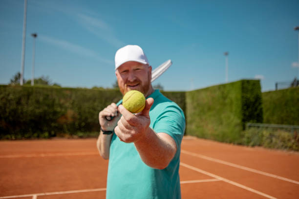 Overweight redhead senior man on the tennis clay court as a form of exercise