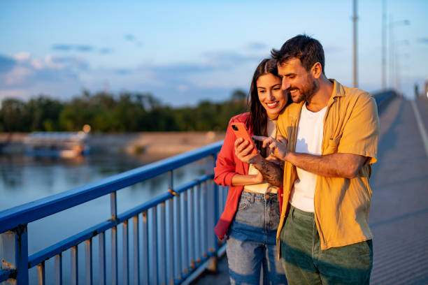 Couple checking phone together on a sunset bridge.