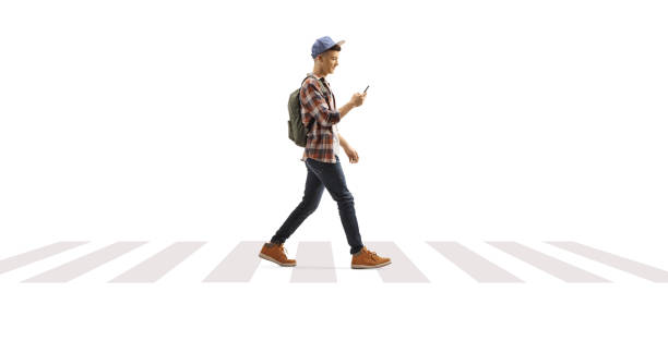istock Guy with a backpack and cap walking and looking at mobile phone at a pedestrian crossing 2161480456