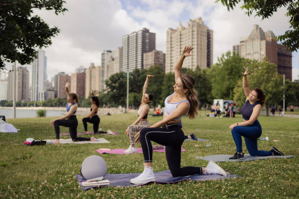 Group of young women attending to a yoga class outdoors in the morninh with New Chicago cityscape on their background. They are meditating and relaxing.