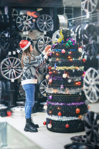 A girl decorates a tire Christmas tree in an auto shop, showing her creative holiday spirit stock photo
