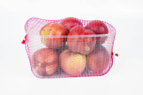 Plastic container of nectarines covered with red mesh in supermarket. Fresh juicy nectarines in plastic package to sell at farmer market isolated on white background. Empty copy space. Selective focus