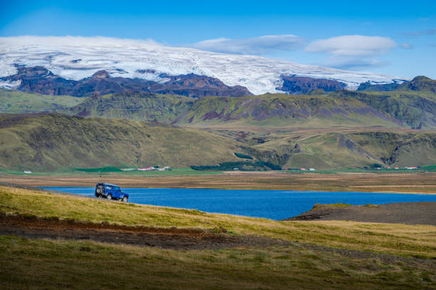 Southern Iceland's landscape while wandering the ring road, a SUV going down the hill on a sunny summer day, Eyjafjallajokull in the background