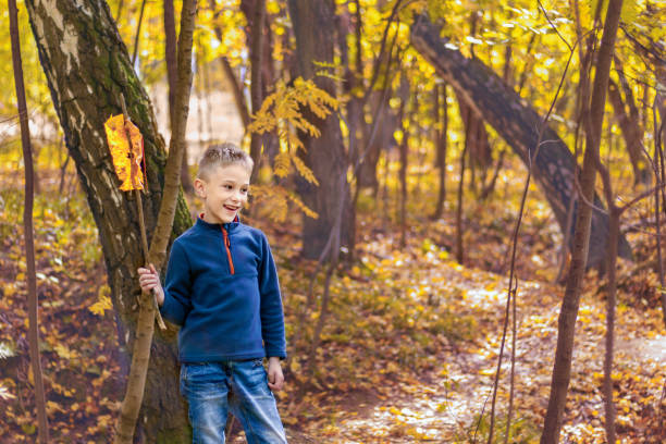 Lively boy in fall woods playing by making flag from stick and leaf. Copy space.