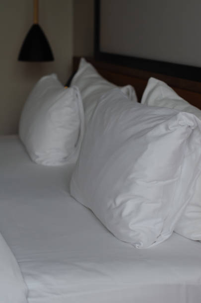 White pillows on white sheets. Wooden headboard in Background