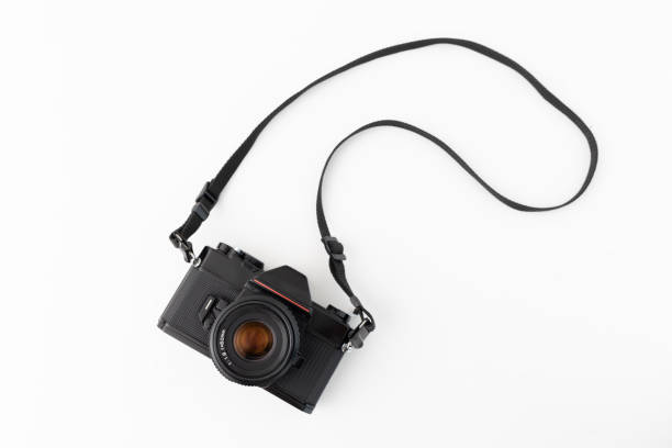 The image shows a black classic SLR camera with a black strap, isolated on a white surface. The camera is viewed from above, providing a clear and detailed perspective. This symbolic image represents photography, camera technology, and retro aesthetics. It is perfect for topics related to photography, technology, vintage products, and creative projects