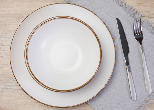 istock Round empty white ceramic plate, knife and fork on the table, top view 2161528120