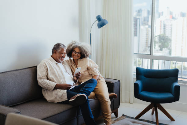 Mature couple surfing the web on smartphone while sitting on sofa at home