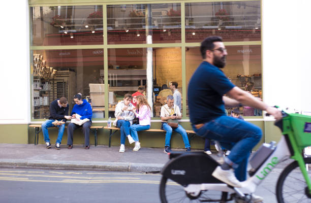 Paris, France: A man rides a bike past Le Pain Retrouvé, a bakery on Rue des Martyrs in the 9th arrondissement as young couples relax and eat breakfast on a bench outside.