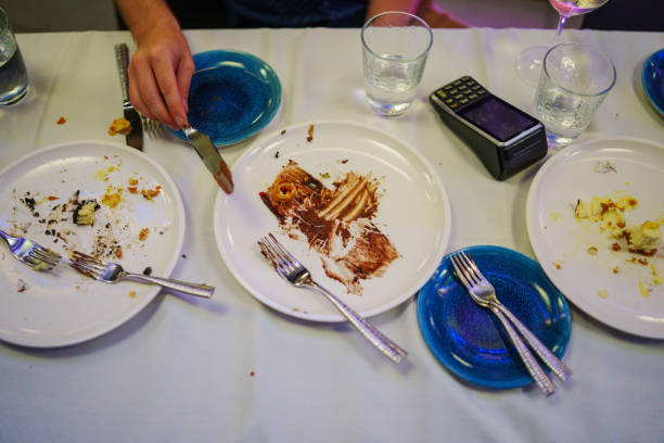 A restaurant worker is cleaning up the used plates from patrons after an evening dinner. We can only see hands and a payment device.