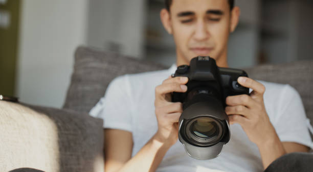 istock Young photographer setting his dslr camera while sitting on sofa 2161541472
