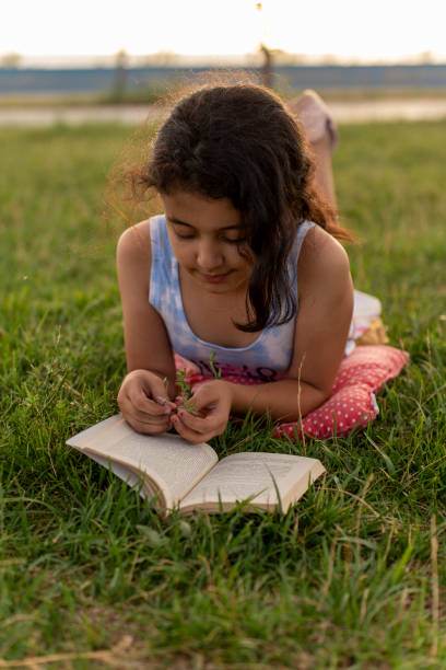 istock Little girl reading book in grass. 2161541728