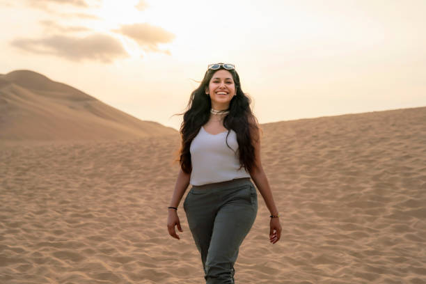 Young Latina woman enjoying the sand dunes at Huacachina Oasis in Ica, Peru, during sunset, smiling and having fun.