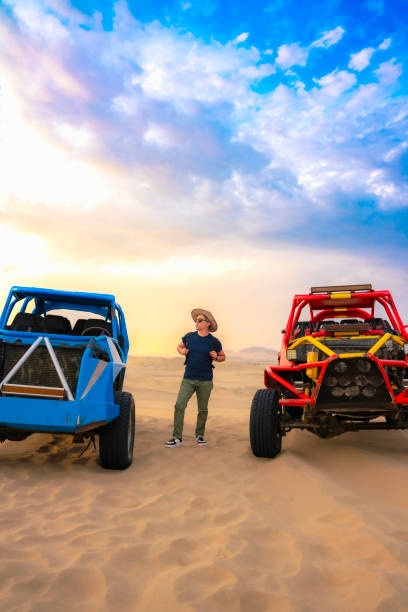 Young man standing confidently on a colorful dune buggy in the Huacachina desert, Ica, Peru, ready for an adventure.