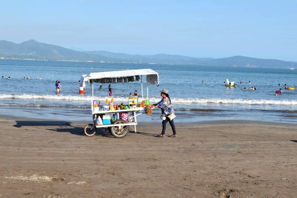 San Blas, Mexico - May 25 2024: A woman is pushing a mobile stand on Islitas beach. The cart is filled with food and drinks. The beach is crowded with people enjoying the day